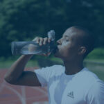 black athlete drinking more water from a bottle during training on the running track