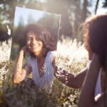 Woman looking in the mirror in nature and mirror smiling back