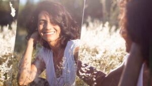 Woman looking in the mirror in nature and mirror smiling back